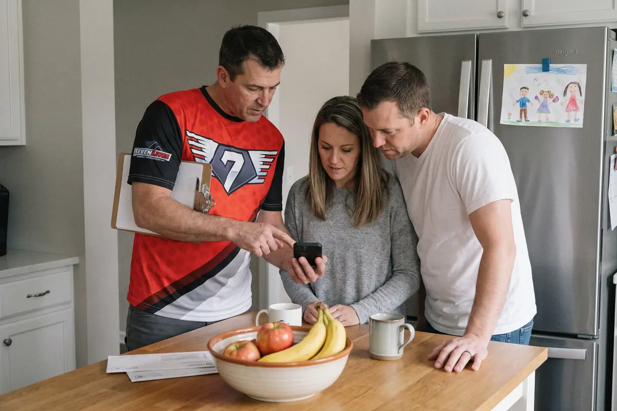 A contractor showing a couple the estimate on a phone at their kitchen island.