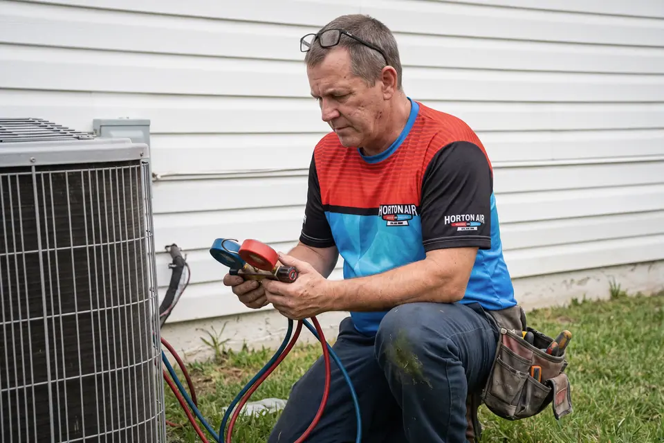 An HVAC technician checking gauges beside an outdoor air conditioner