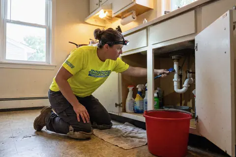 A plumber in a headlamp fixing the drain pipes under a kitchen sink