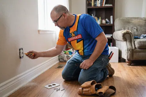 An electrician wiring a wall outlet in a living room
