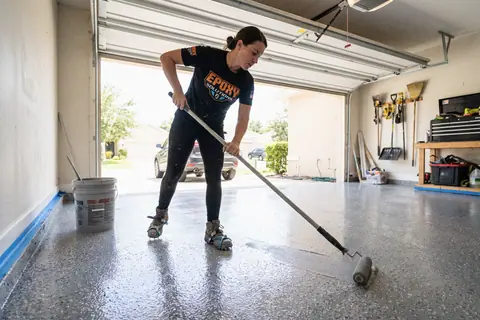 A floor-coating installer rolling epoxy across a garage floor