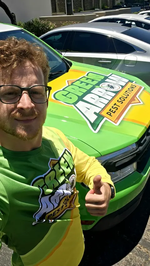 A pest-control professional beside his Green Arrow Pest Solutions service vehicle