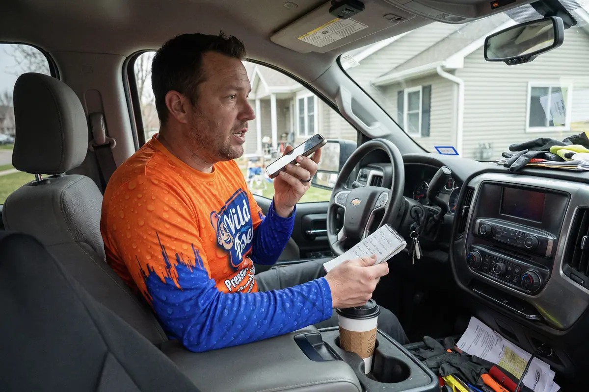 A pressure washing business owner in his truck recording a voicemail greeting from a notepad.
