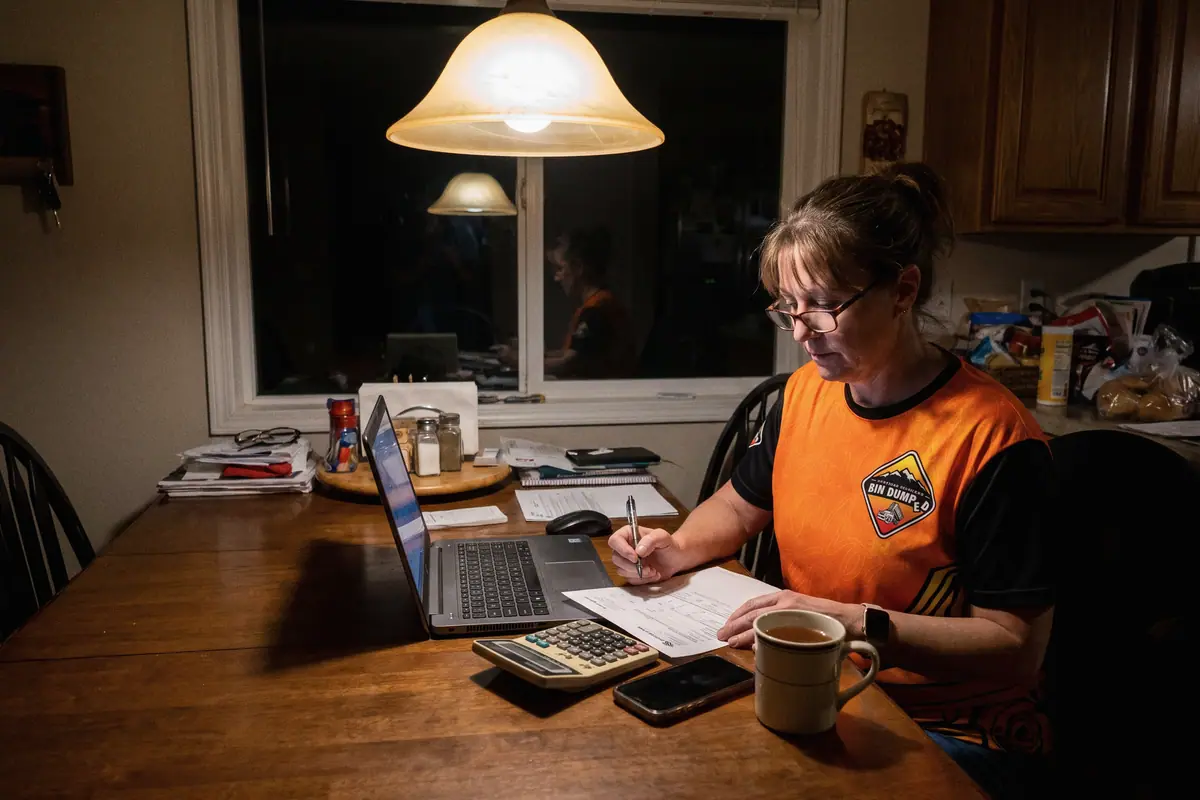 An owner at the kitchen table late in the evening with invoices, a laptop and a calculator.